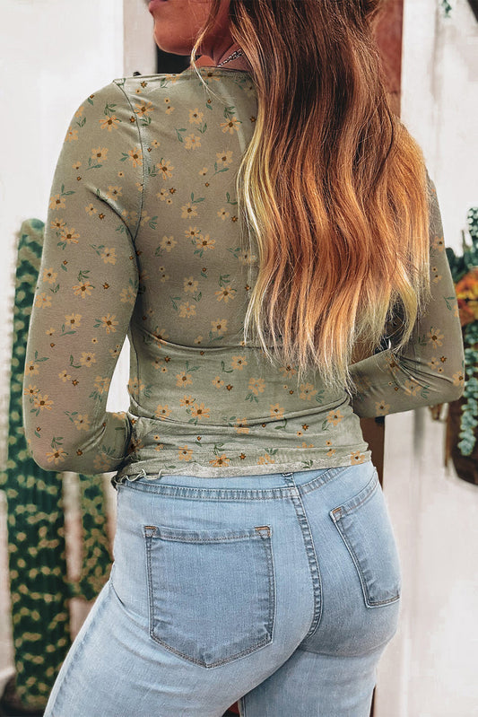 Person wearing a green floral long-sleeve top and light blue jeans with a blurred background.