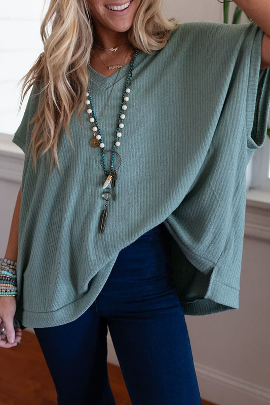 Woman wearing a green top and blue jeans with a necklace, indoors.