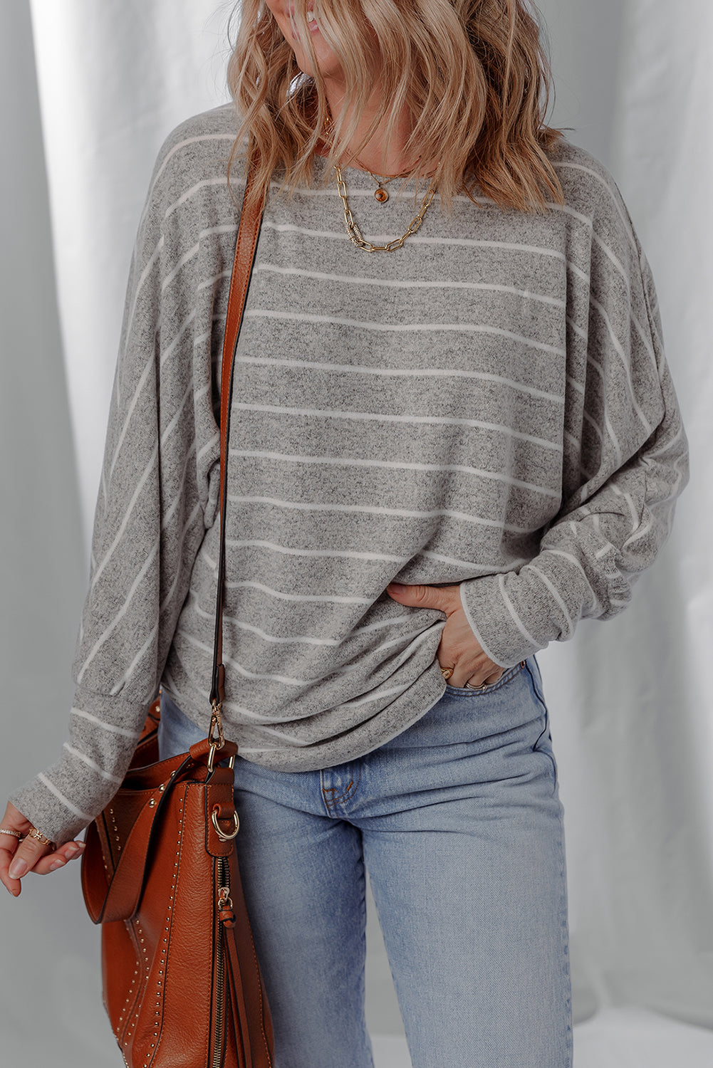 Person wearing a gray striped sweater and blue jeans, holding a brown leather bag against a white background
