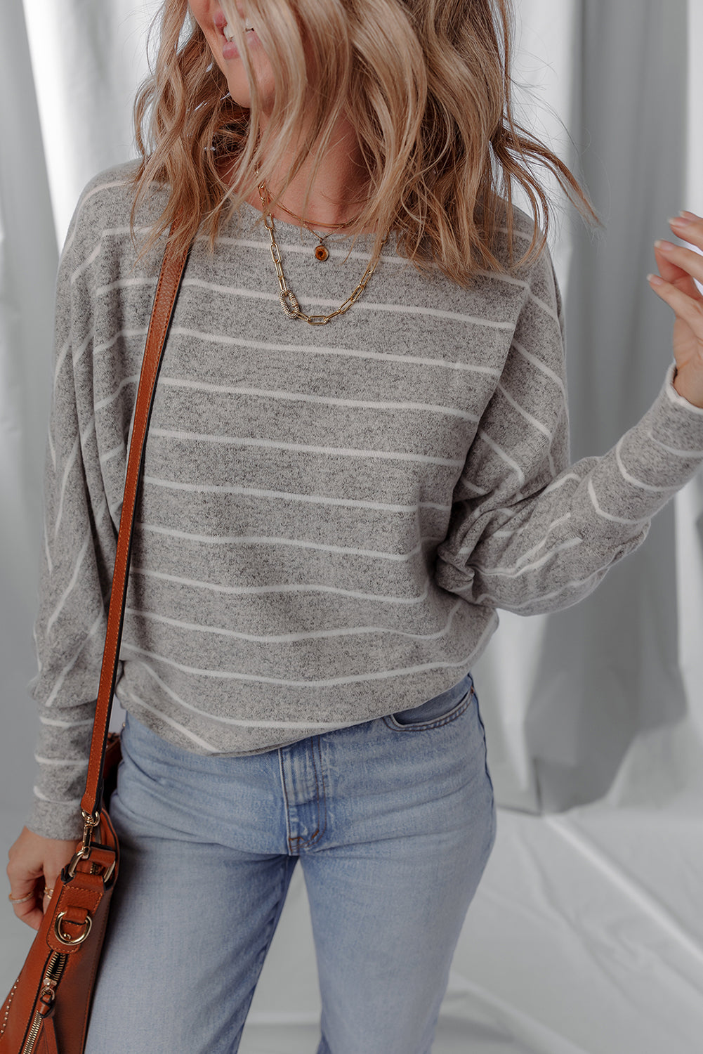 Person wearing a gray striped sweater and blue jeans with a brown leather bag against a white background