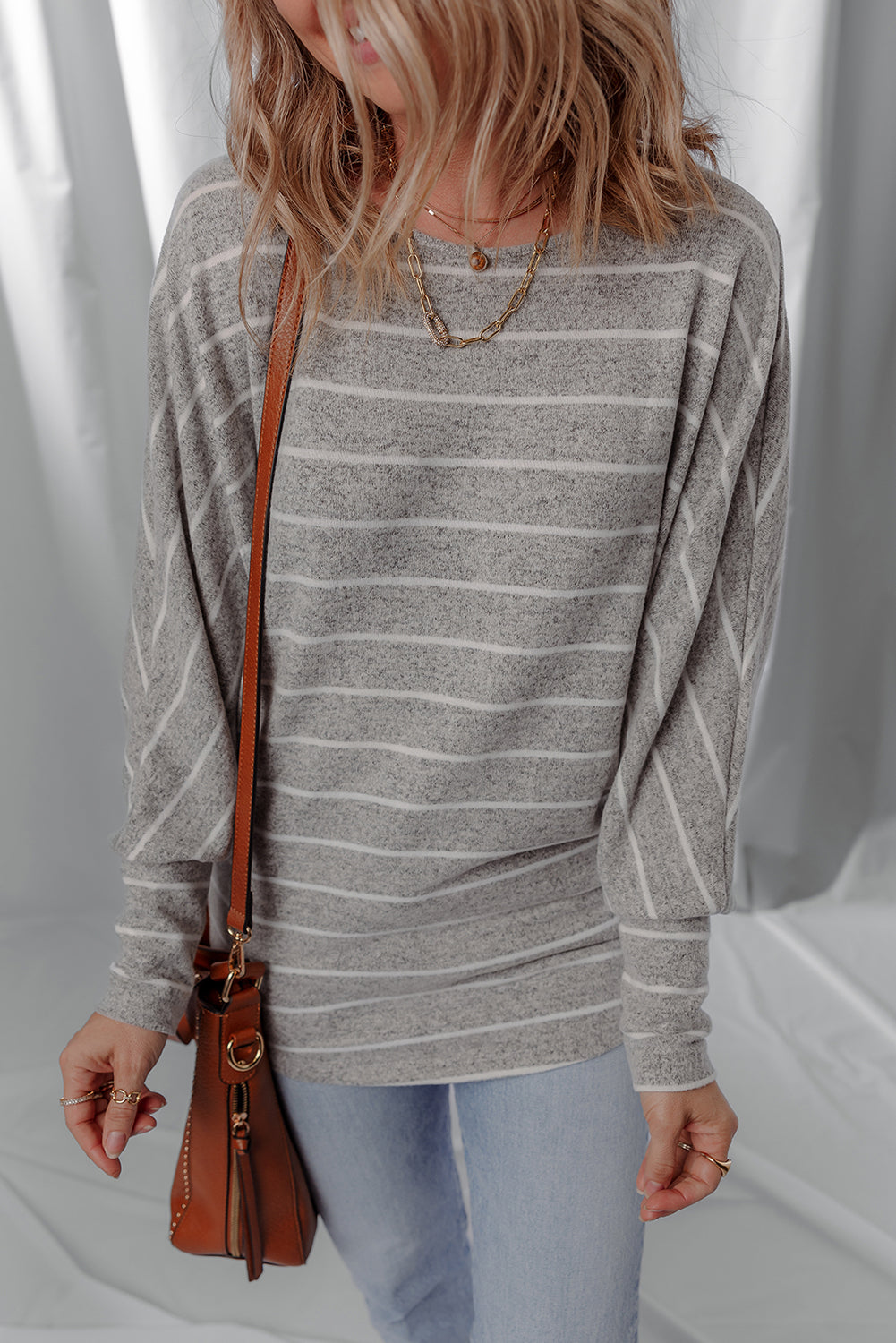 Person wearing a gray striped sweater and light blue jeans, holding a brown leather bag.