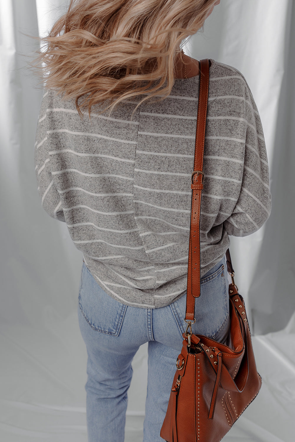 Person wearing a gray striped sweater and blue jeans with a brown leather handbag on a white background