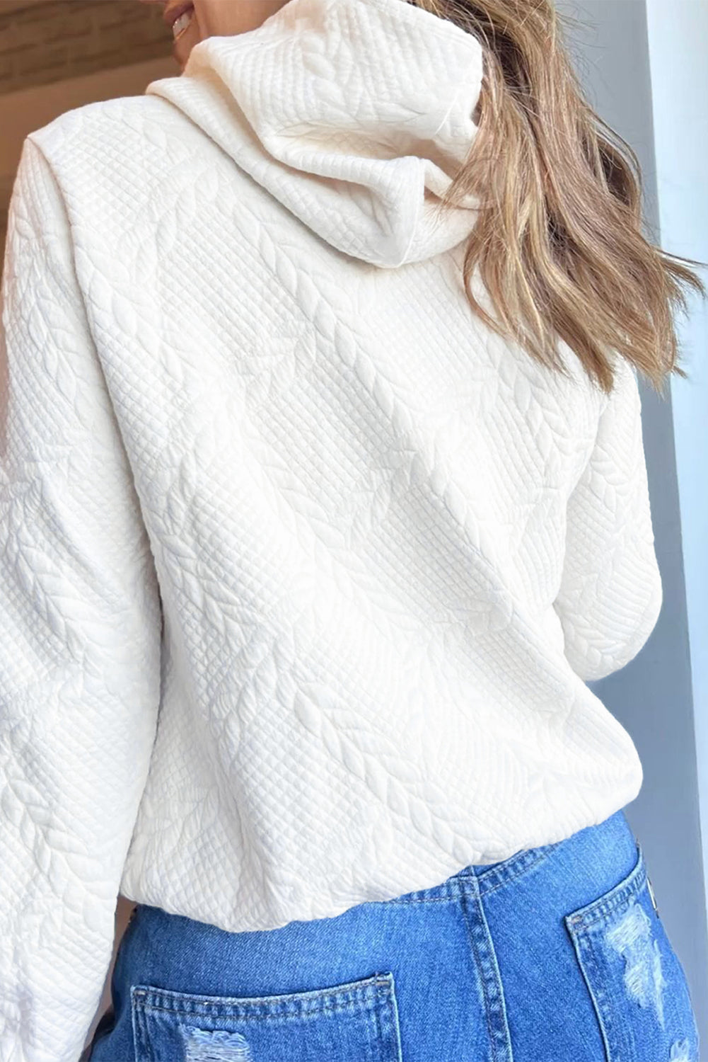 Person wearing a white textured sweater and blue jeans indoors