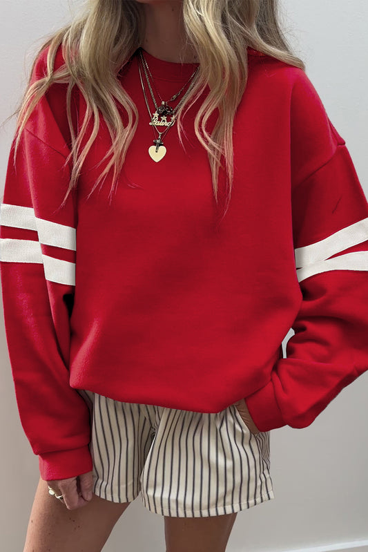 Person wearing a red sweatshirt with white stripes and striped shorts against a plain background