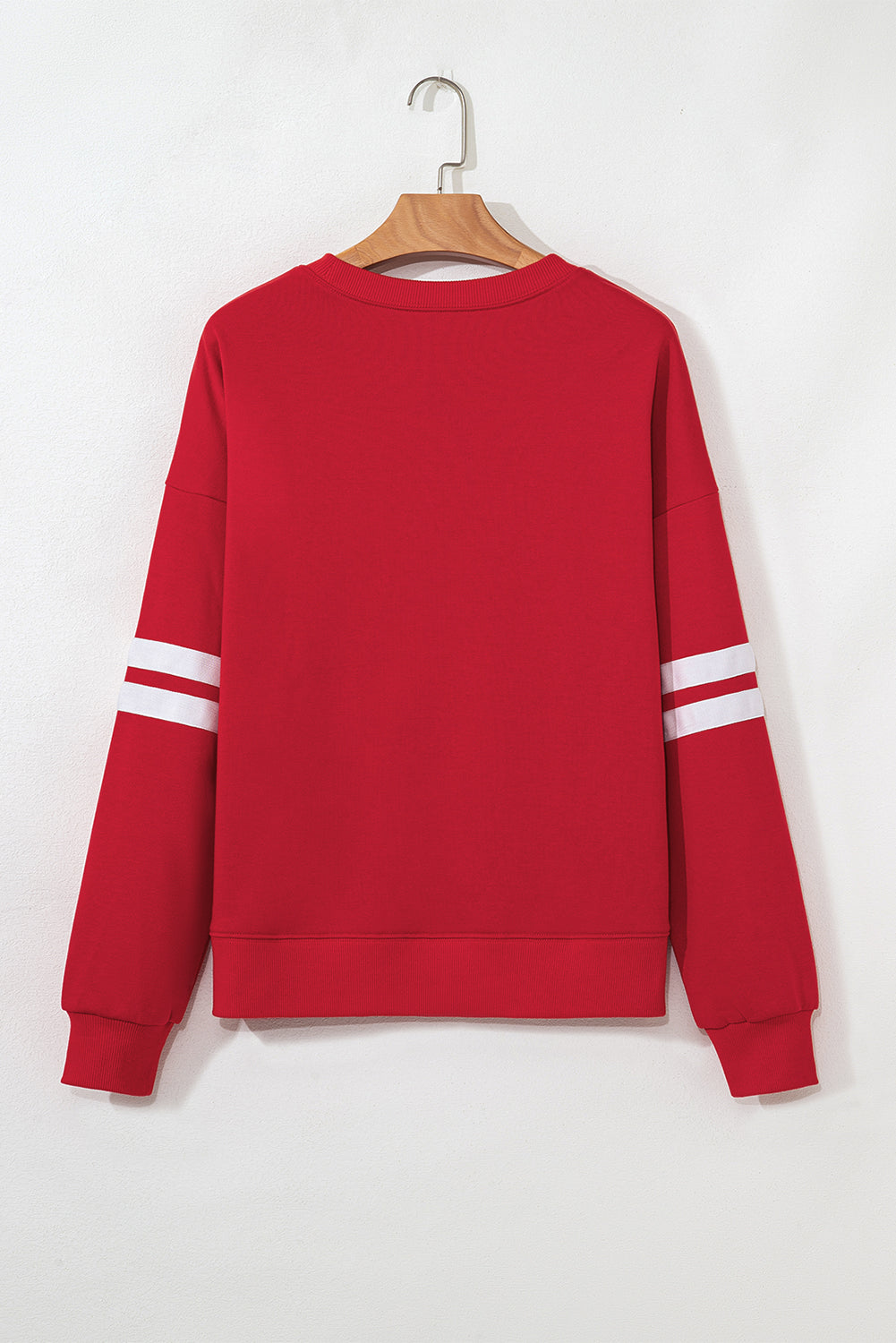 Red sweatshirt with white stripes on sleeves hanging on a wooden hanger against a white background