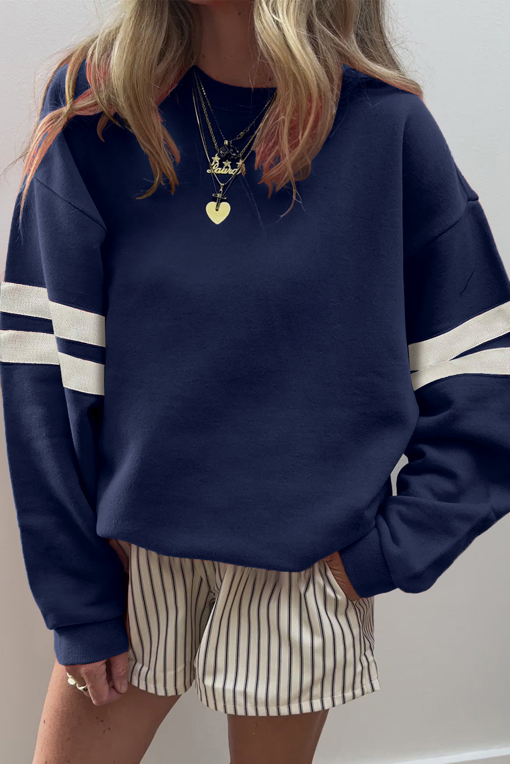 Person wearing a navy blue sweatshirt with white stripes and striped shorts against a plain background