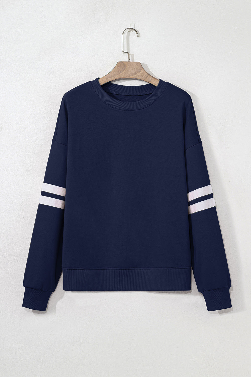 Navy blue sweatshirt with white stripes on sleeves hanging on a wooden hanger against a white background