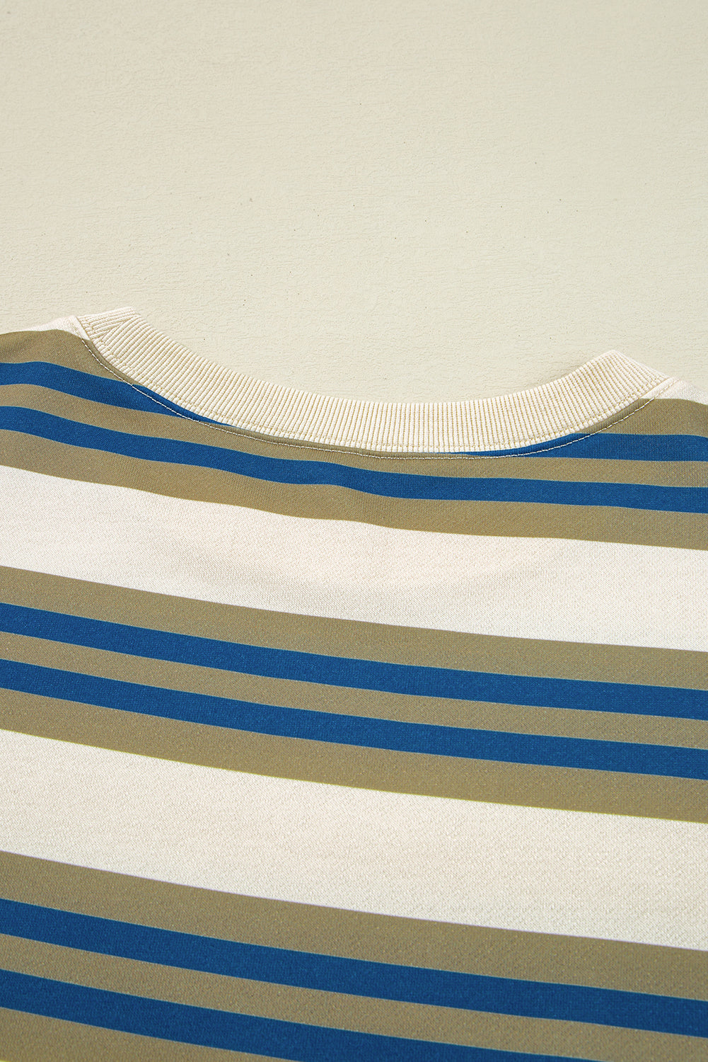Close-up of a striped shirt with blue, green, and white horizontal stripes on a beige background.