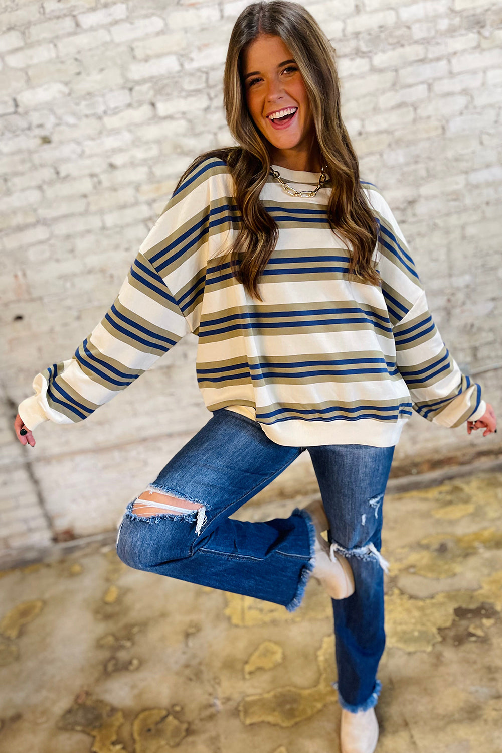 Woman wearing a striped sweater and ripped jeans against a brick wall.