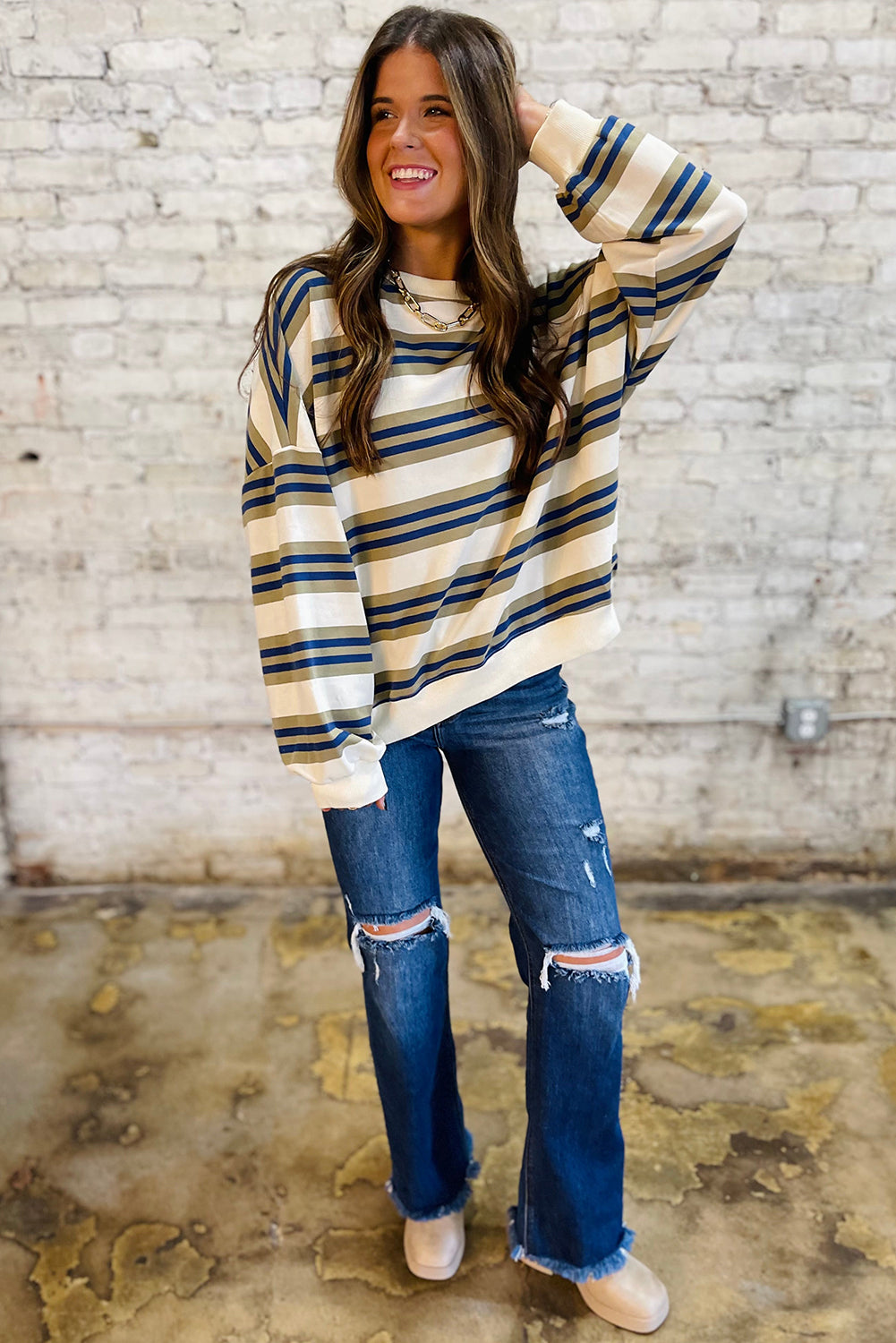 Woman wearing a striped sweater and ripped jeans against a brick wall.