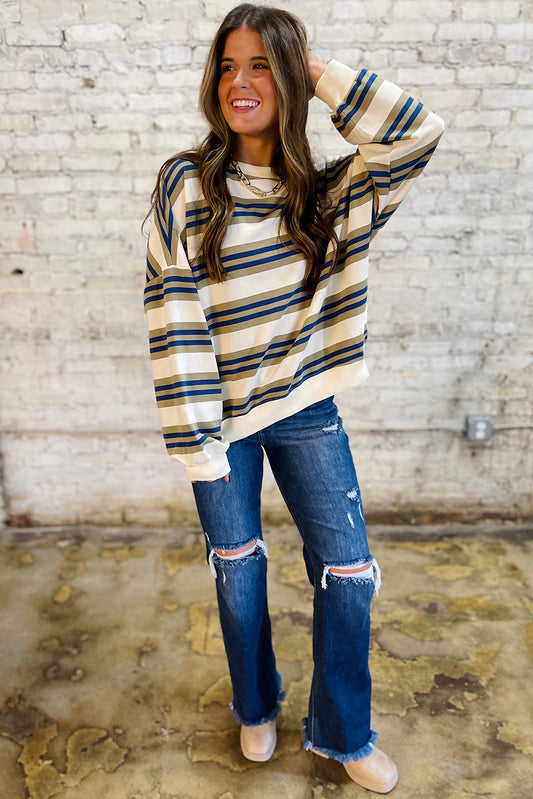 Woman wearing a striped sweater and ripped jeans against a brick wall.
