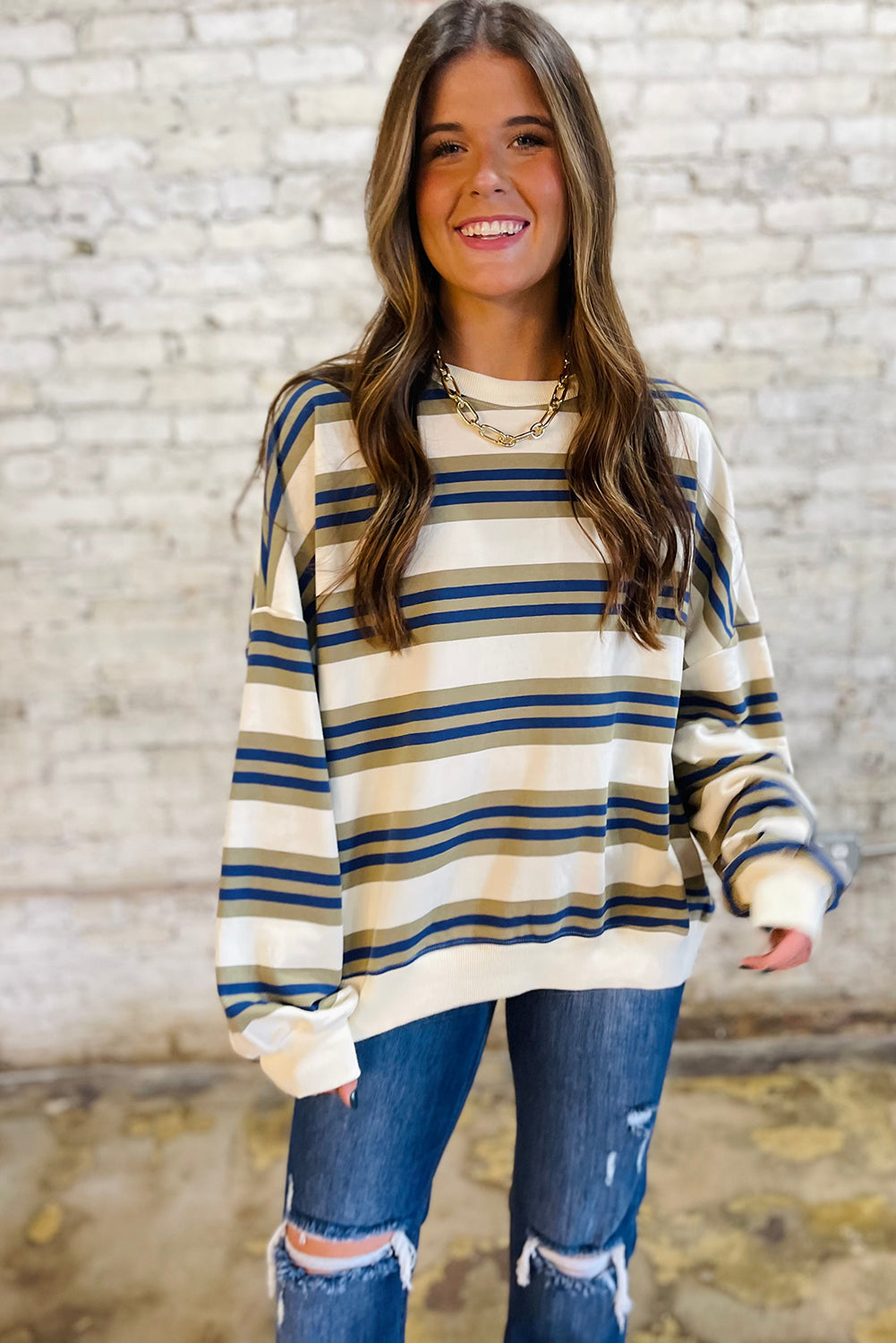 Woman wearing a striped sweater and ripped jeans against a textured wall.