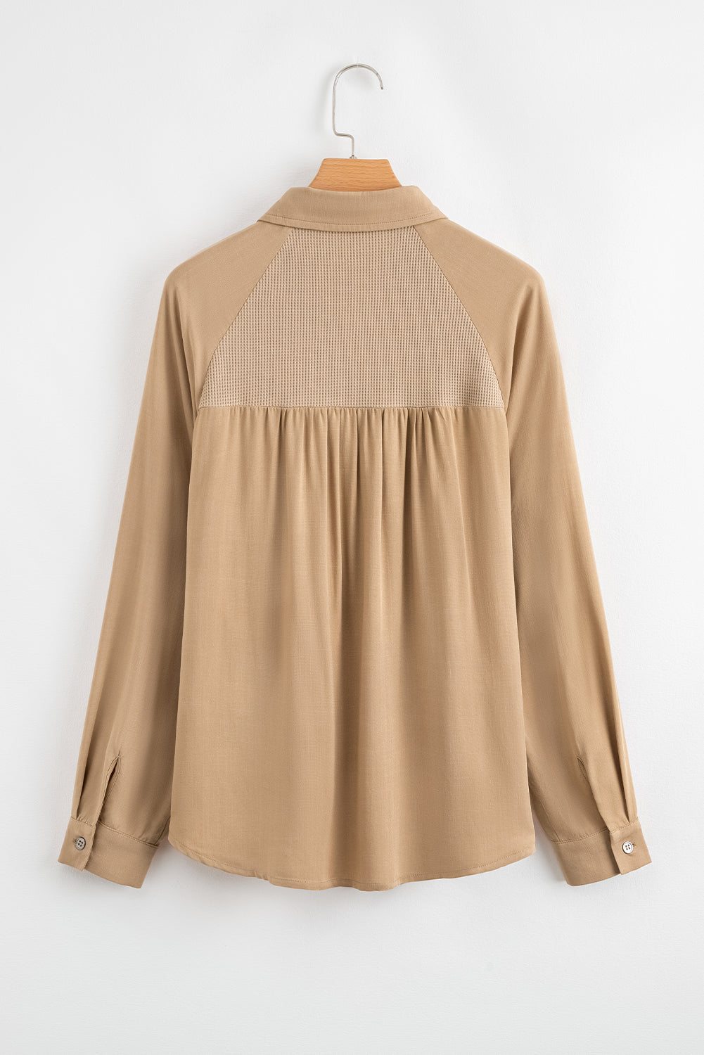 Beige blouse with a textured back panel on a hanger against a white background