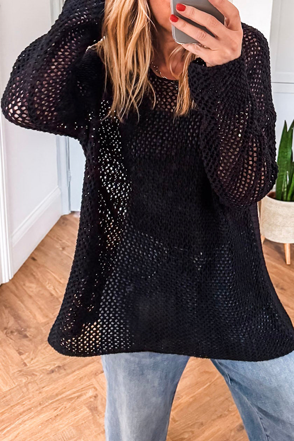 Person wearing a black knit sweater and light blue jeans indoors.
