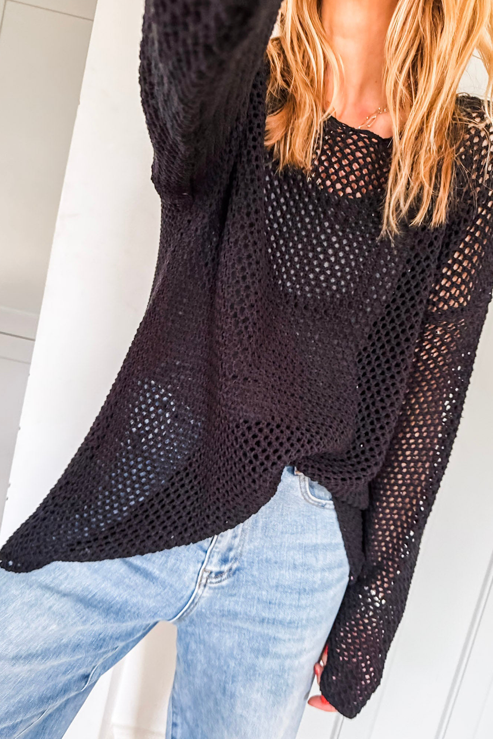 Person wearing a black mesh sweater and blue jeans against a white background