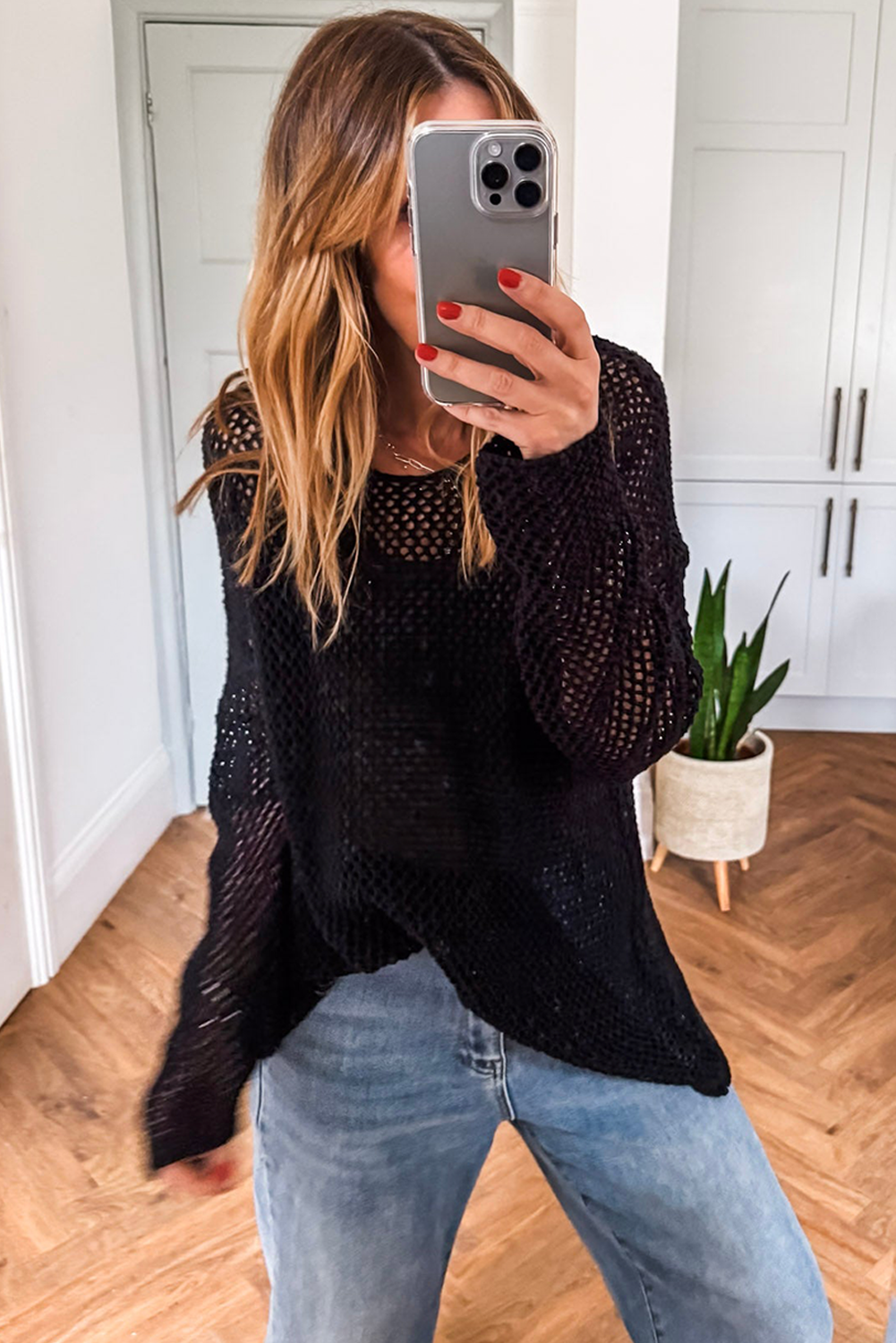 Person wearing a black knit cardigan and light blue jeans, taking a mirror selfie.