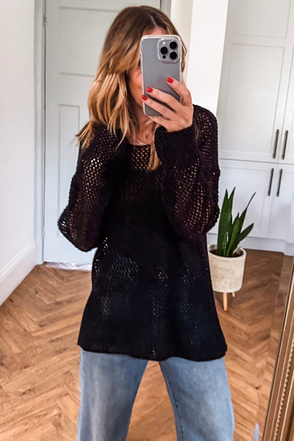 Person wearing a black textured sweater and light blue jeans taking a mirror selfie.