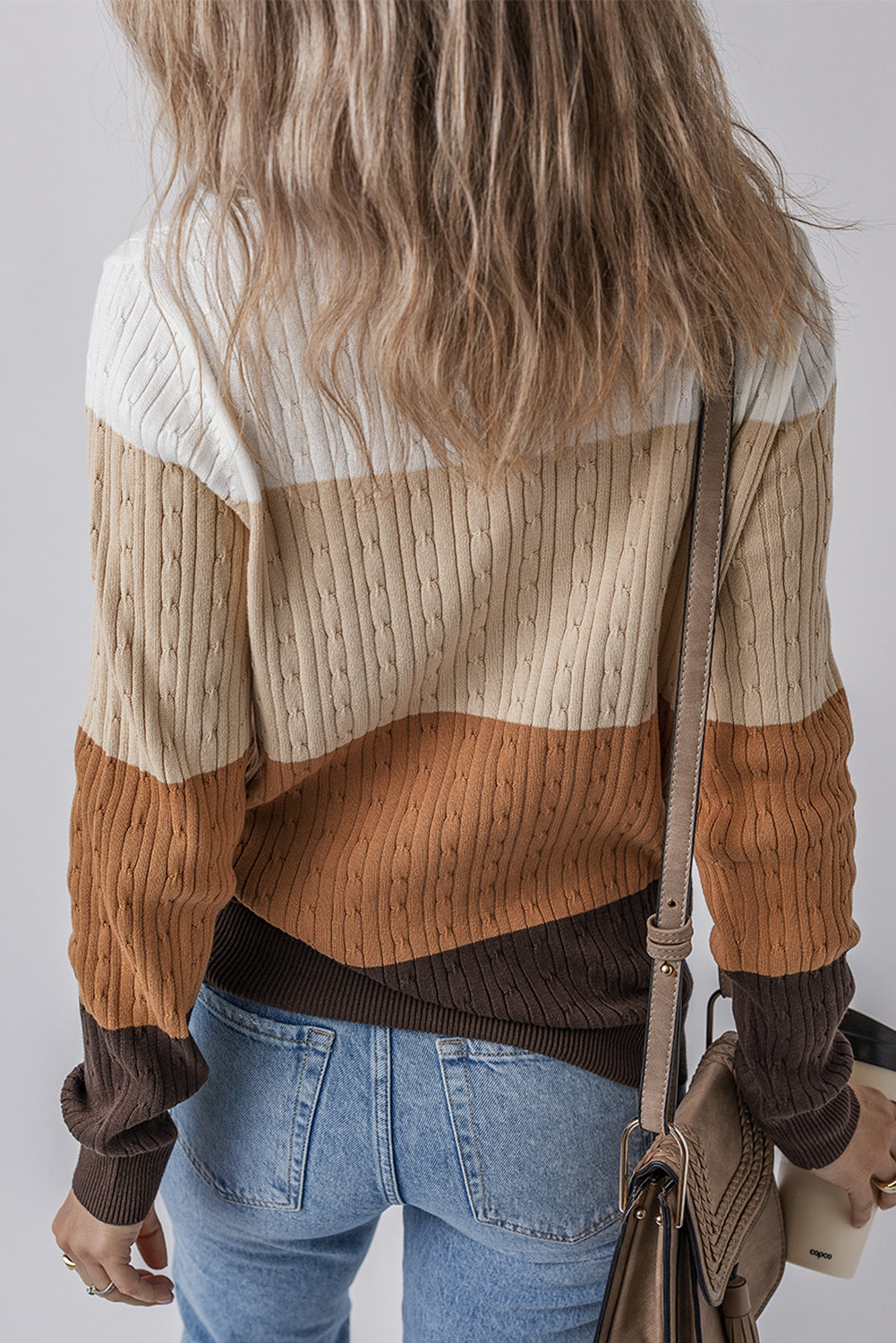 Person wearing a striped sweater and jeans with a neutral background