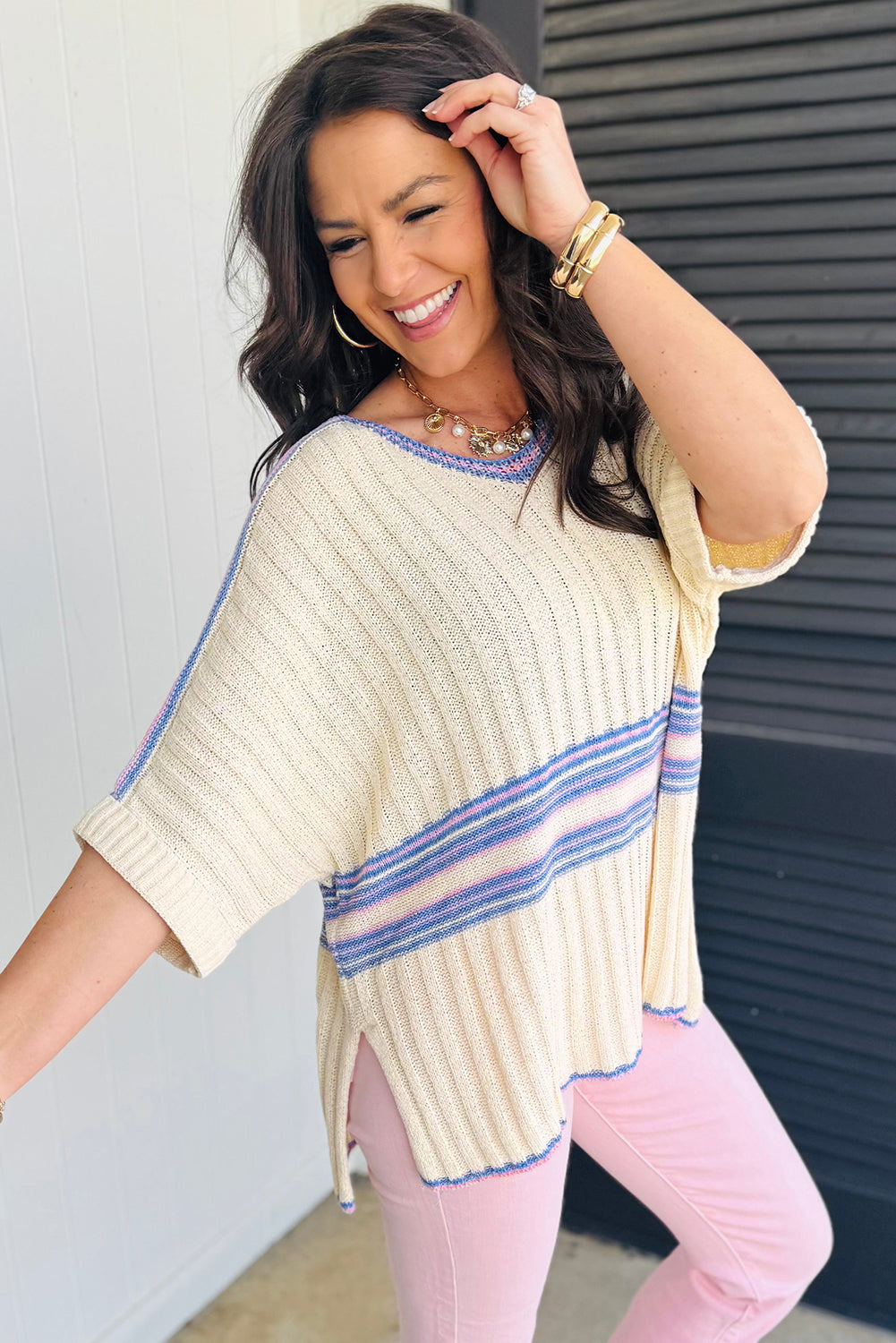 Woman wearing a cream-colored poncho with blue stripes and pink pants against a gray wall.