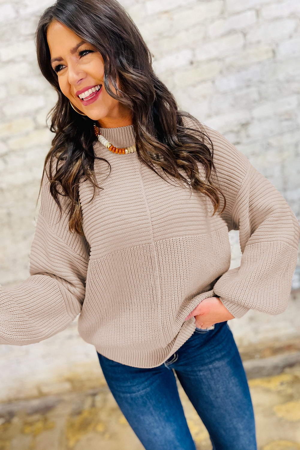 Woman wearing a beige sweater and blue jeans against a stone wall background