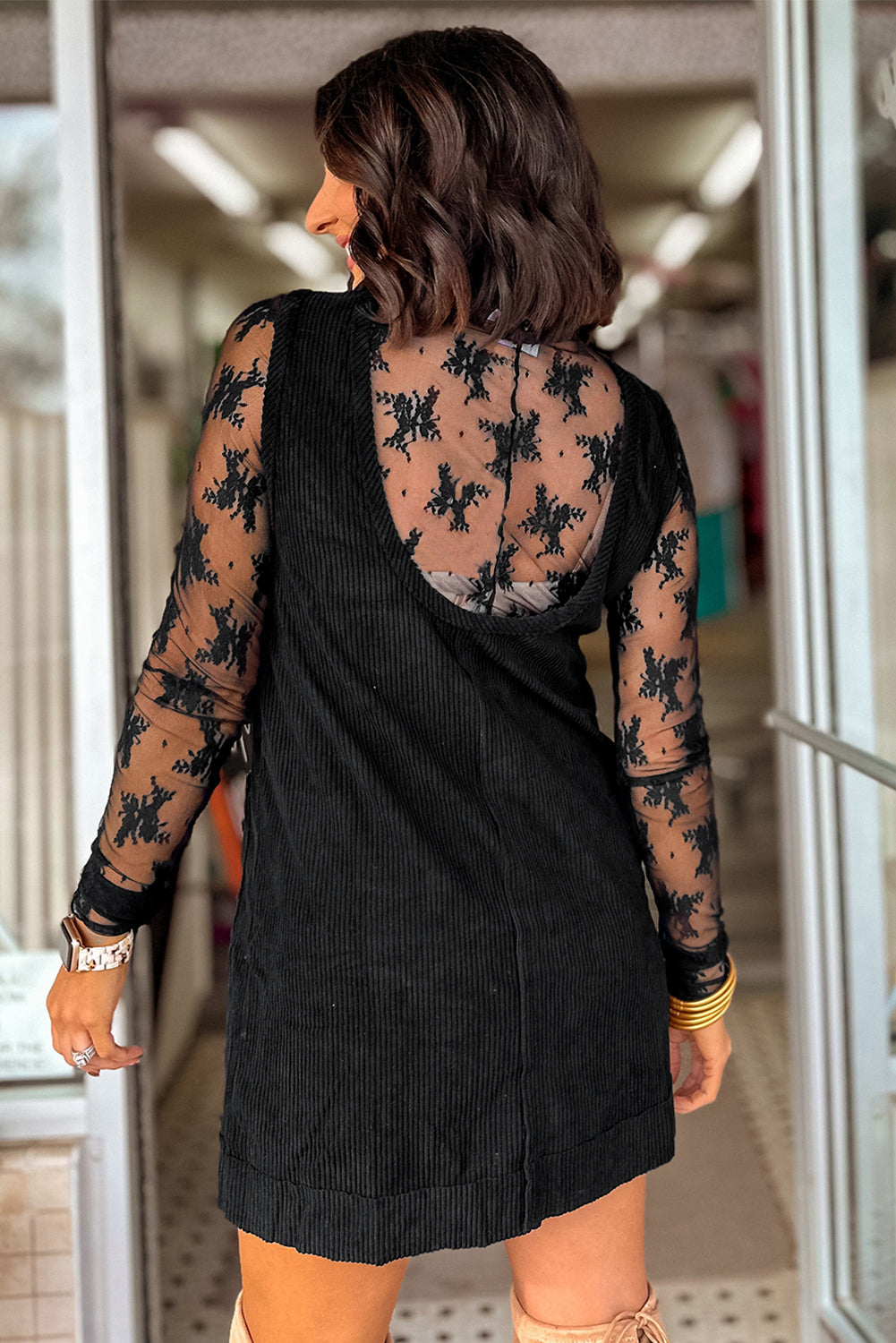 Woman wearing a black dress with sheer sleeves and floral patterns in a reflective surface setting