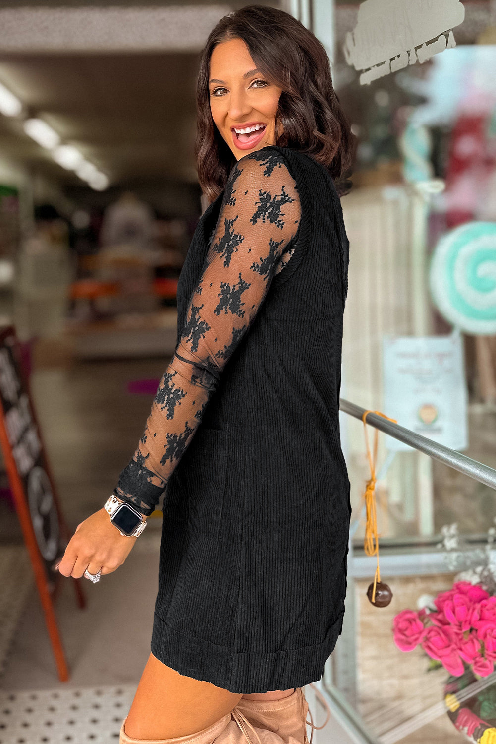 Woman wearing a black dress with floral lace sleeves in an indoor setting.