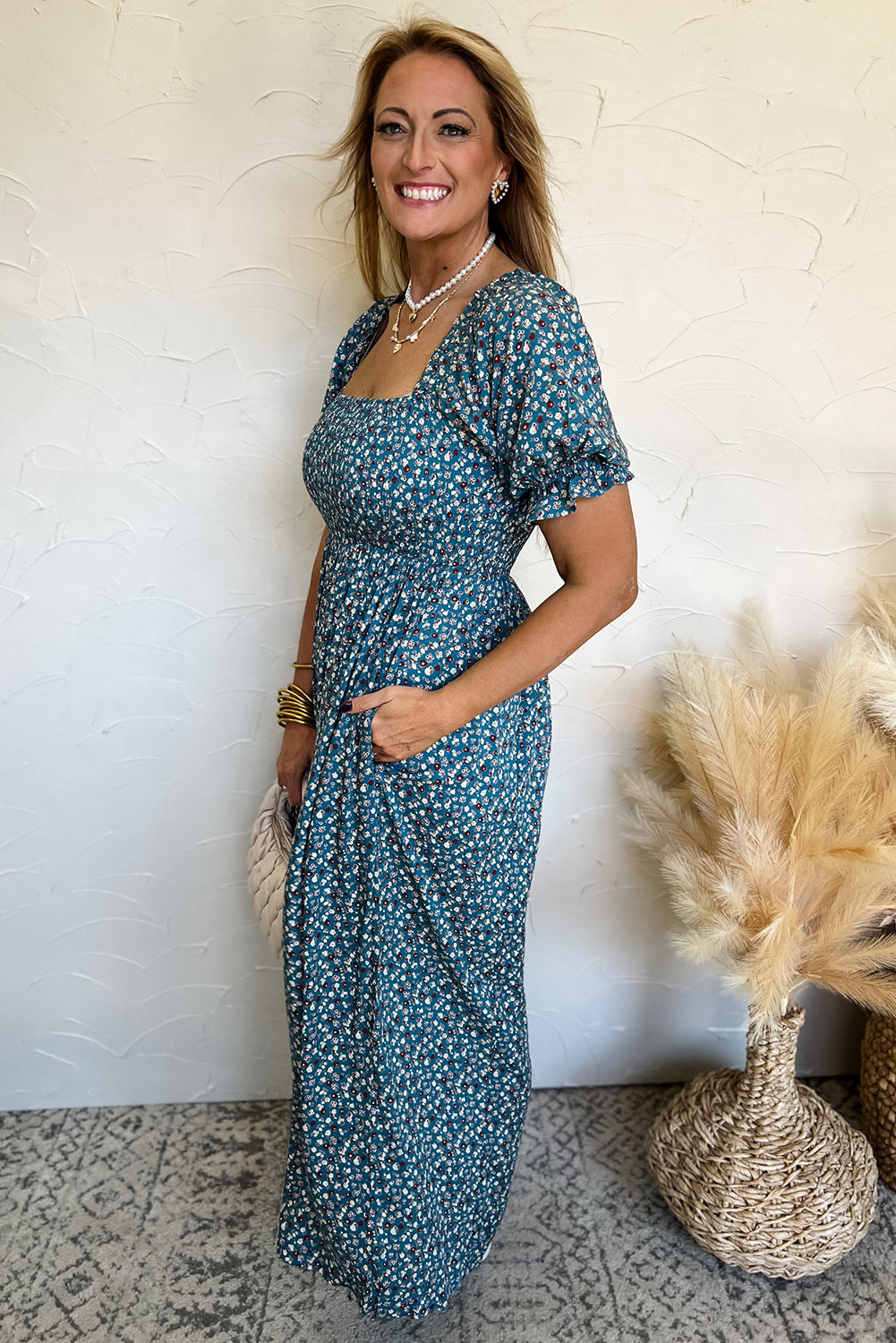 Woman wearing a blue floral dress standing against a white wall with decorative elements.