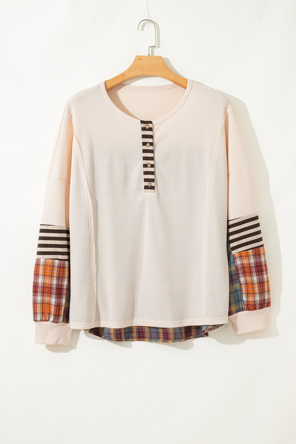 Beige sweater with plaid sleeves on a hanger against a white background