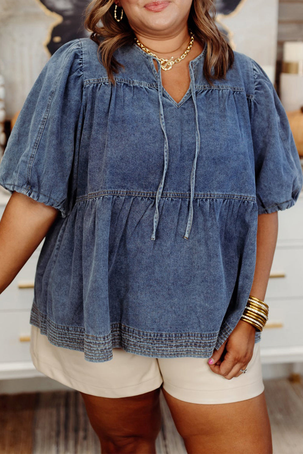 Woman wearing a denim blouse and beige shorts indoors.