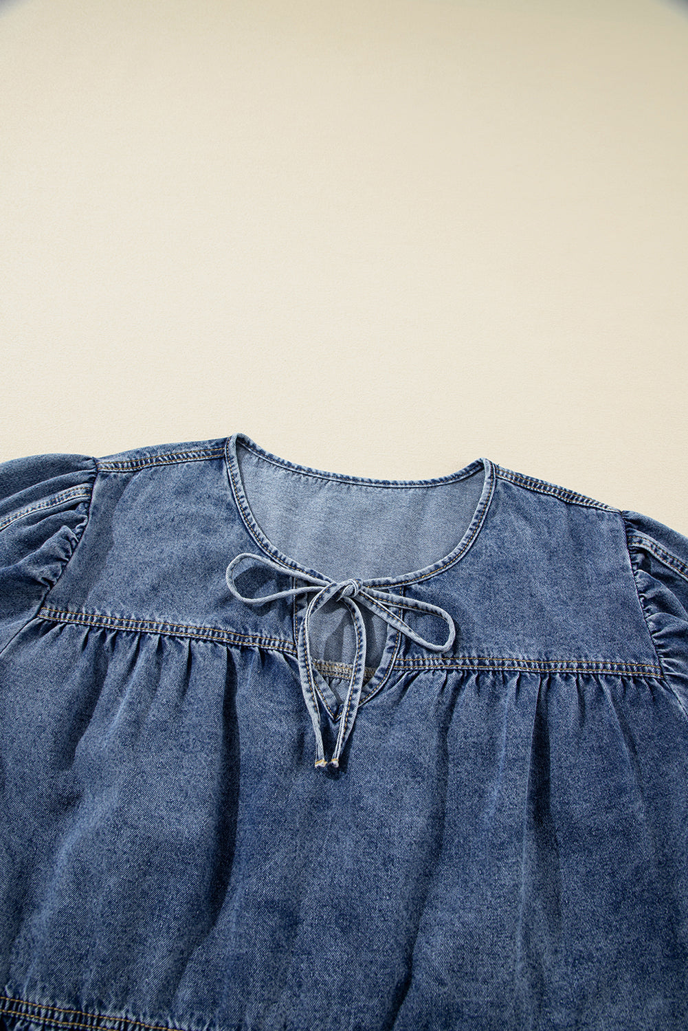 Blue denim top with ruffled sleeves and tie detail on a beige background
