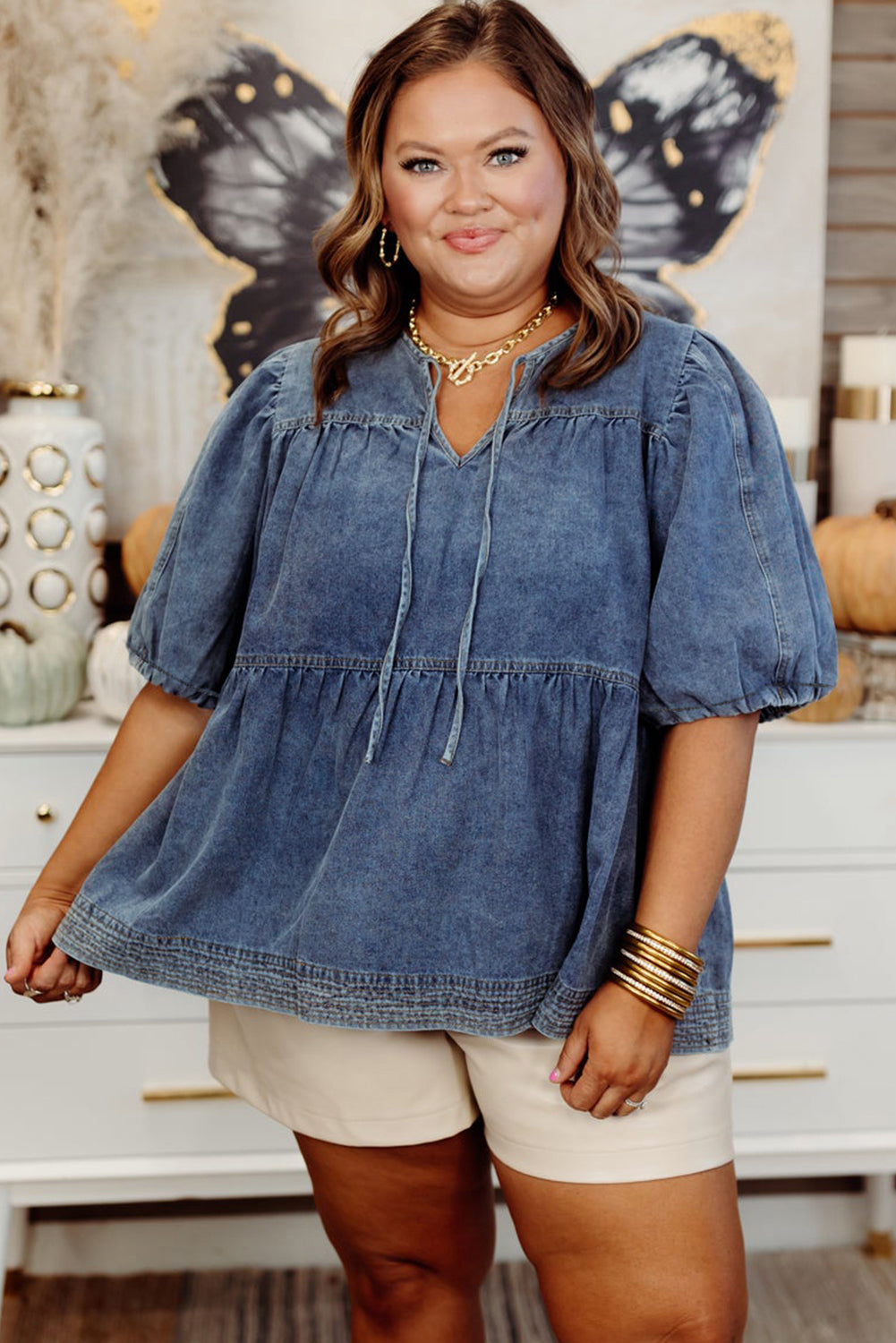 Woman wearing a denim top and beige shorts in a home setting with decorative items.