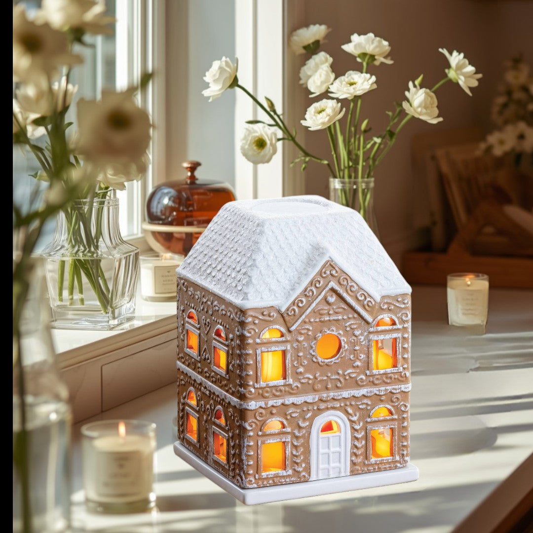 Gingerbread House Fragrance Warmer with white roof and illuminated windows.