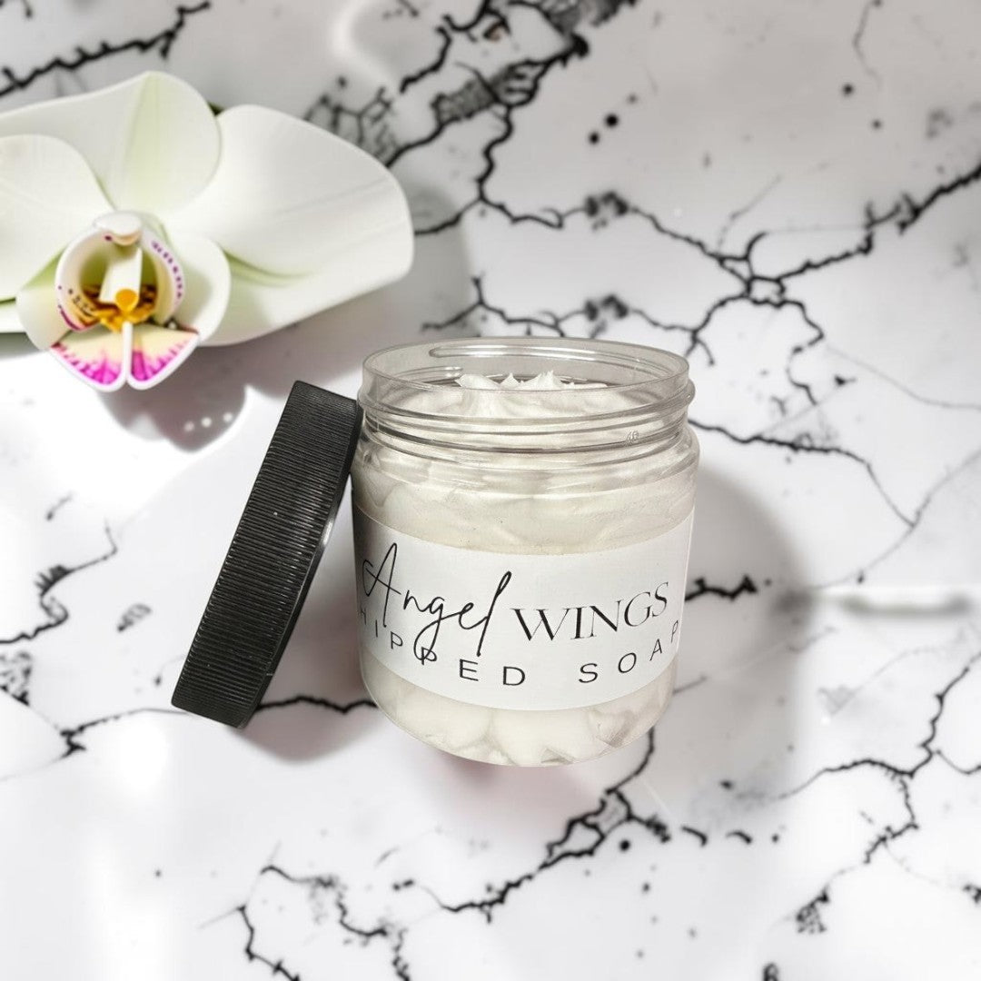 Doodlations Angel Wings whipped soap in a clear jar with lid off, featuring a fluffy white texture and a label with elegant script.