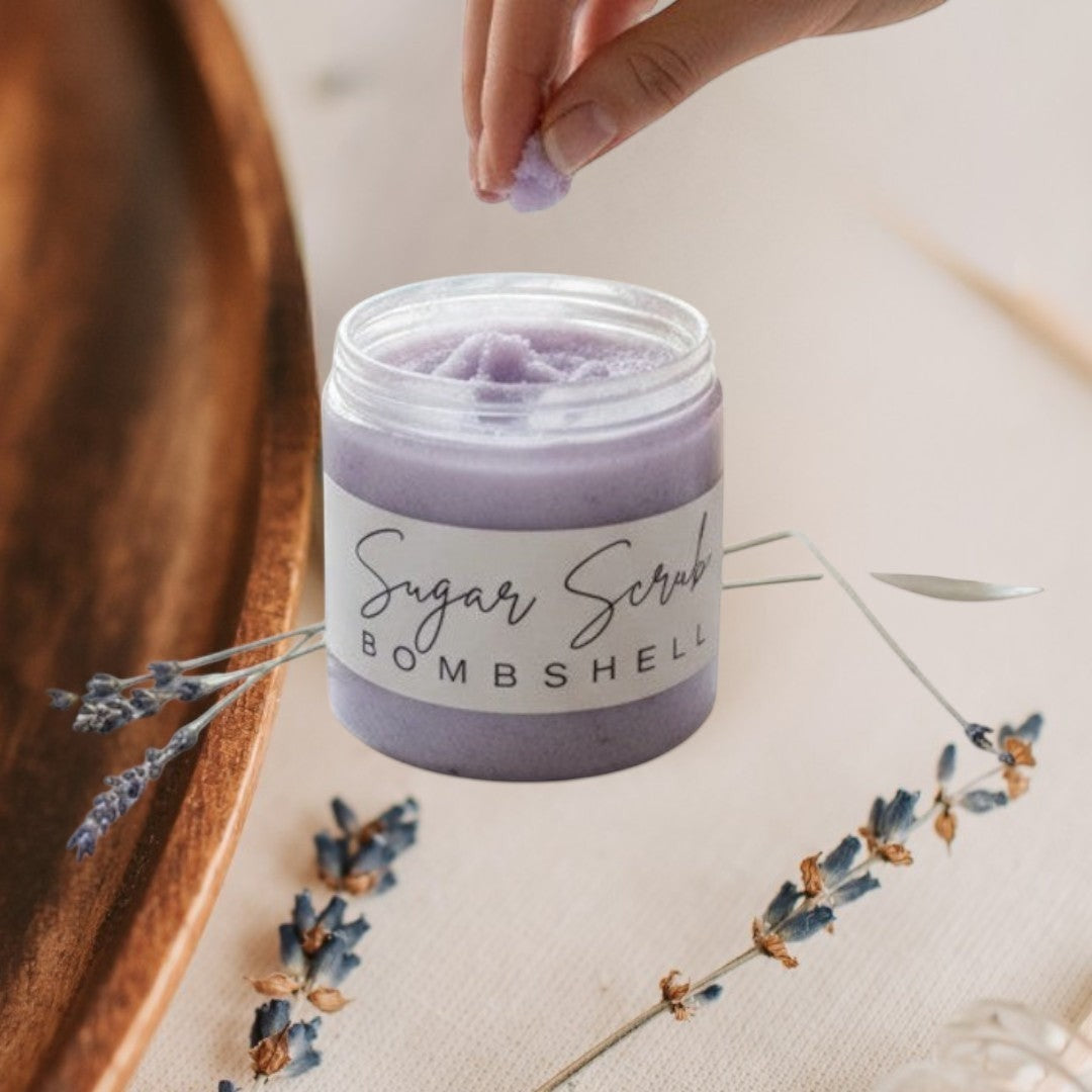 Doodlations Coffee Bar & Boutique Bombshell Sugar Scrub in a clear jar with a black lid. Lavender colored scrub.