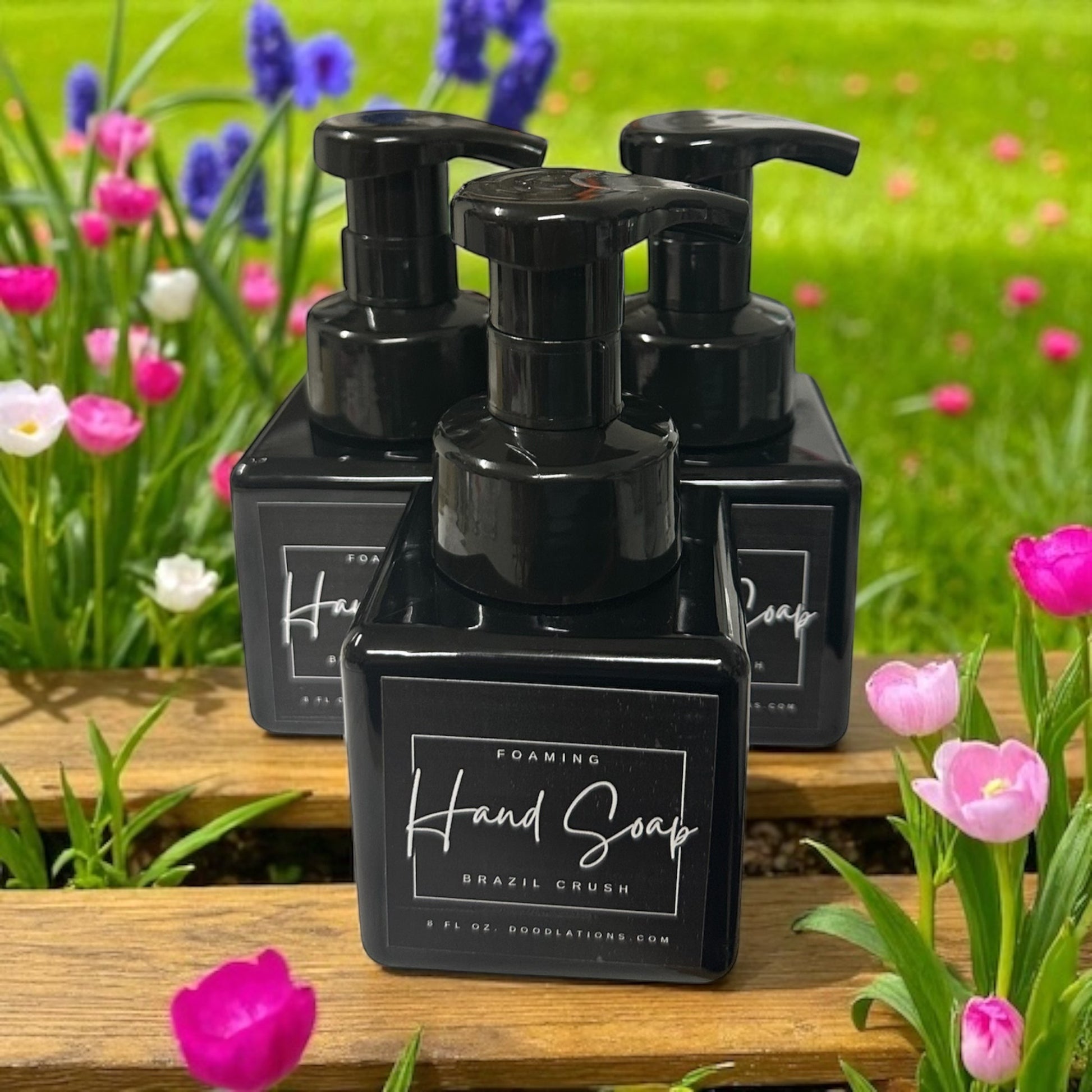 Doodlations Coffee Bar & Boutique Brazilian Crush foaming hand soap in black bottles with pumps, set against a backdrop of colorful flowers.