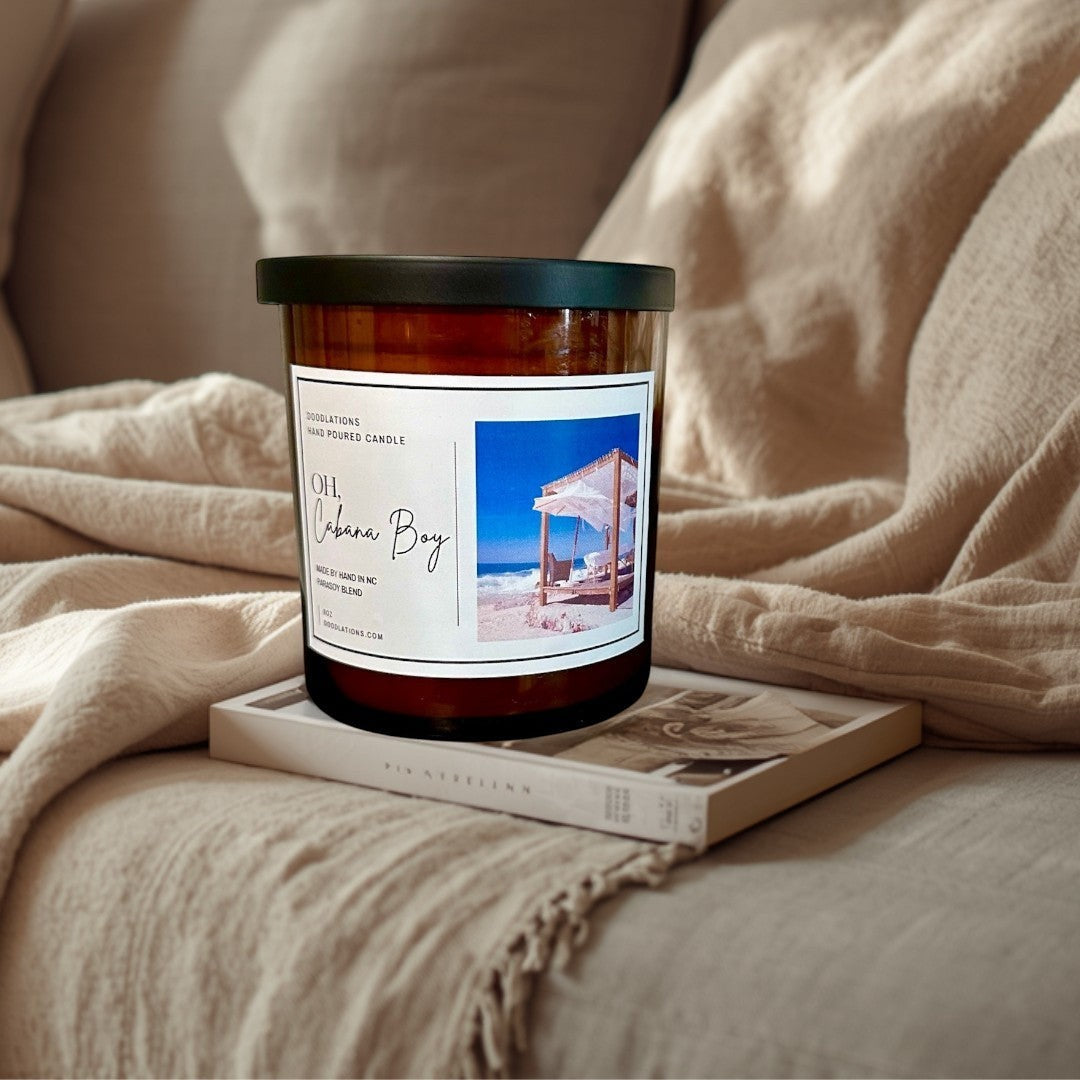 Doodlations Oh Cabana Boy hand-poured soy blend candle in amber glass with a black lid. Tropical beach scene on label.