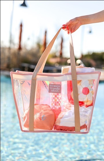 Doodlations Coffee Bar & Boutique clear PVC poolside tote bag with pink faux leather trim and straps, filled with beach essentials.