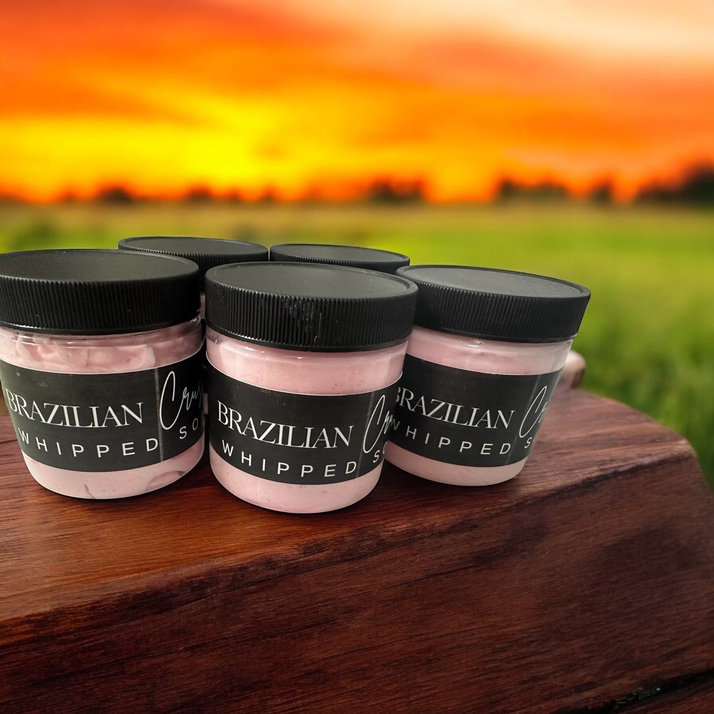 Doodlations Coffee Bar & Boutique Brazilian Crush whipped soap jars with pink cream against a sunset background.