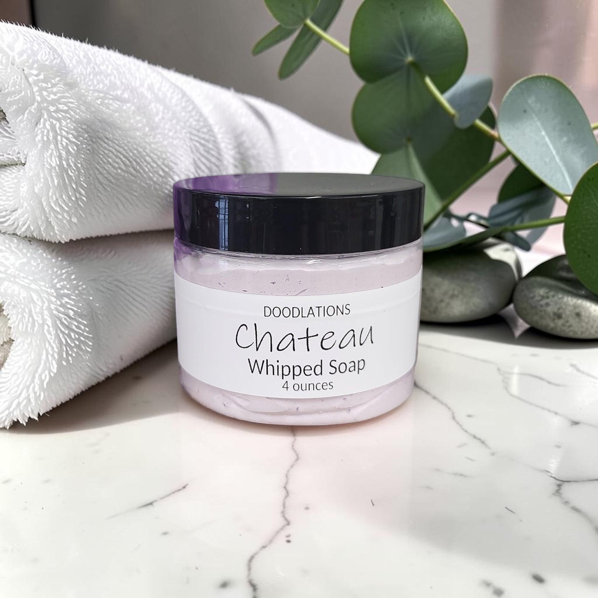 Doodlations Coffee Bar & Boutique Chateau whipped soap in a 4oz jar with a purple loofah on a marble surface.