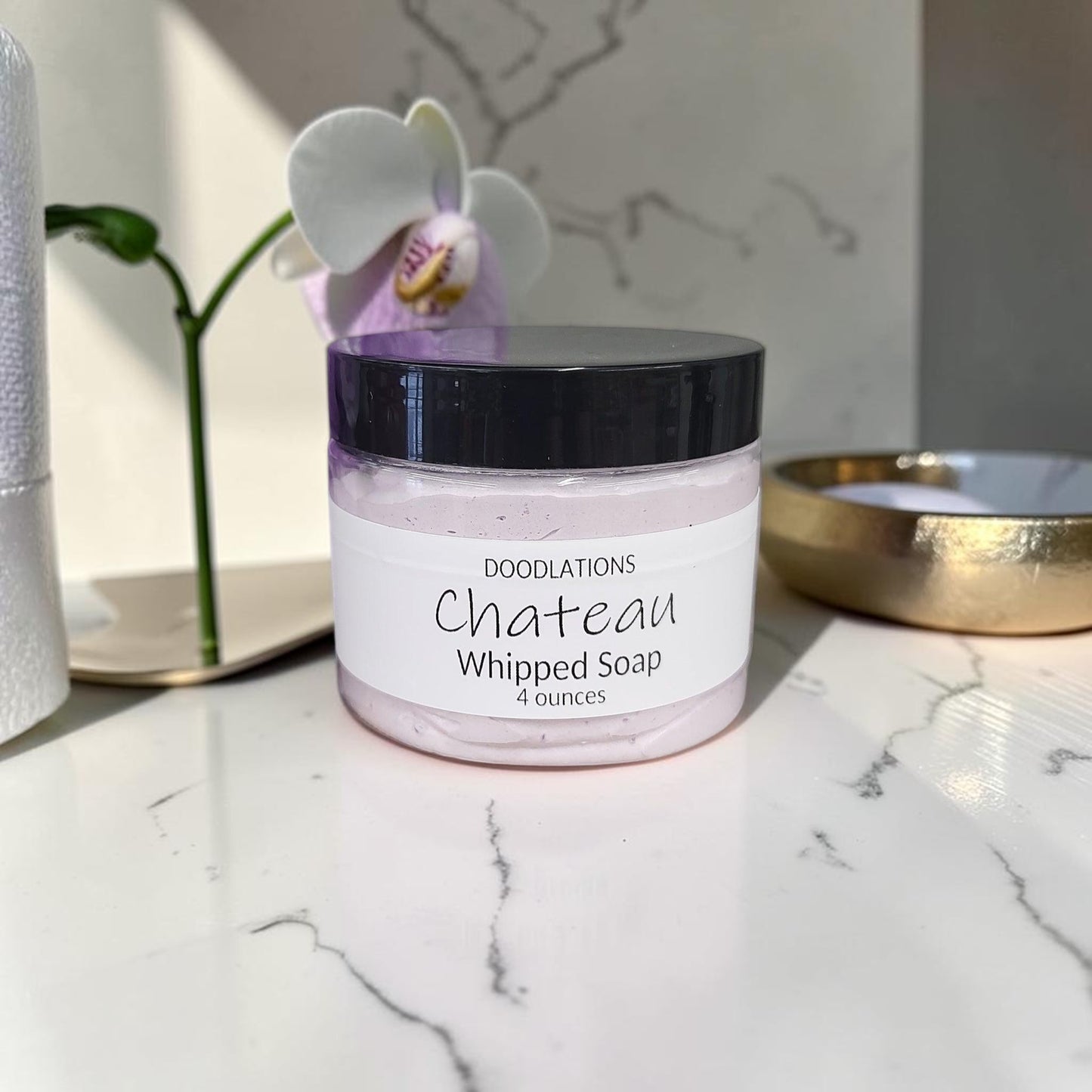 Doodlations Coffee Bar & Boutique Chateau whipped soap in a 4oz jar with a purple bath loofah on a marble surface.
