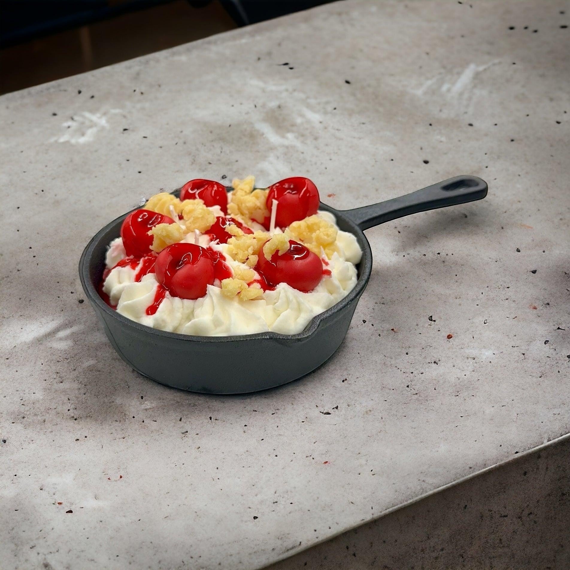 Doodlations Coffee Bar & Boutique Cherry Yum Yum candle in a black iron skillet with white wax frosting, red wax cherries, and crumble topping.