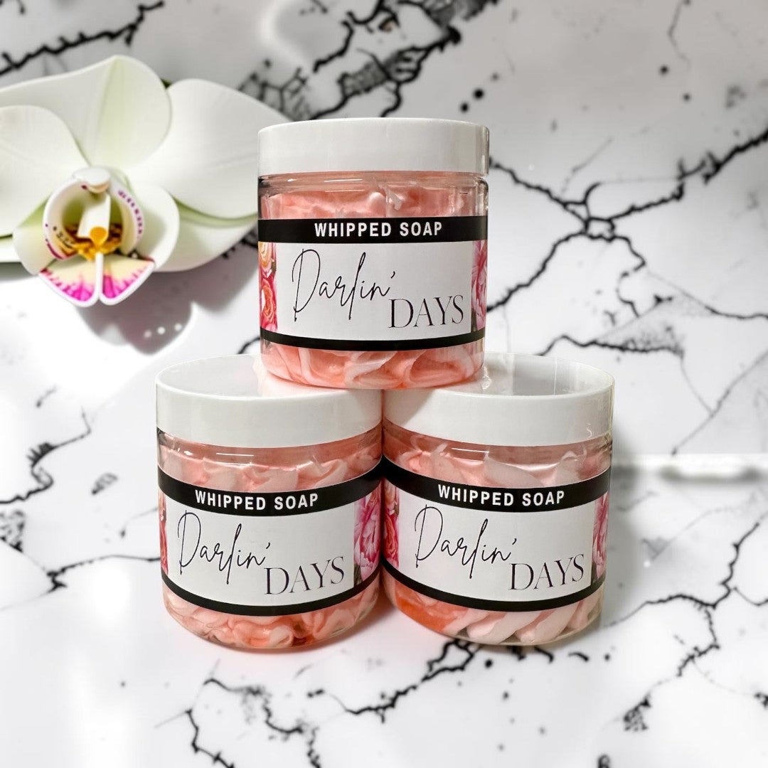 Doodlations Coffee Bar & Boutique Darlin Days whipped soap in clear jars with pink foaming soap against green leaves.