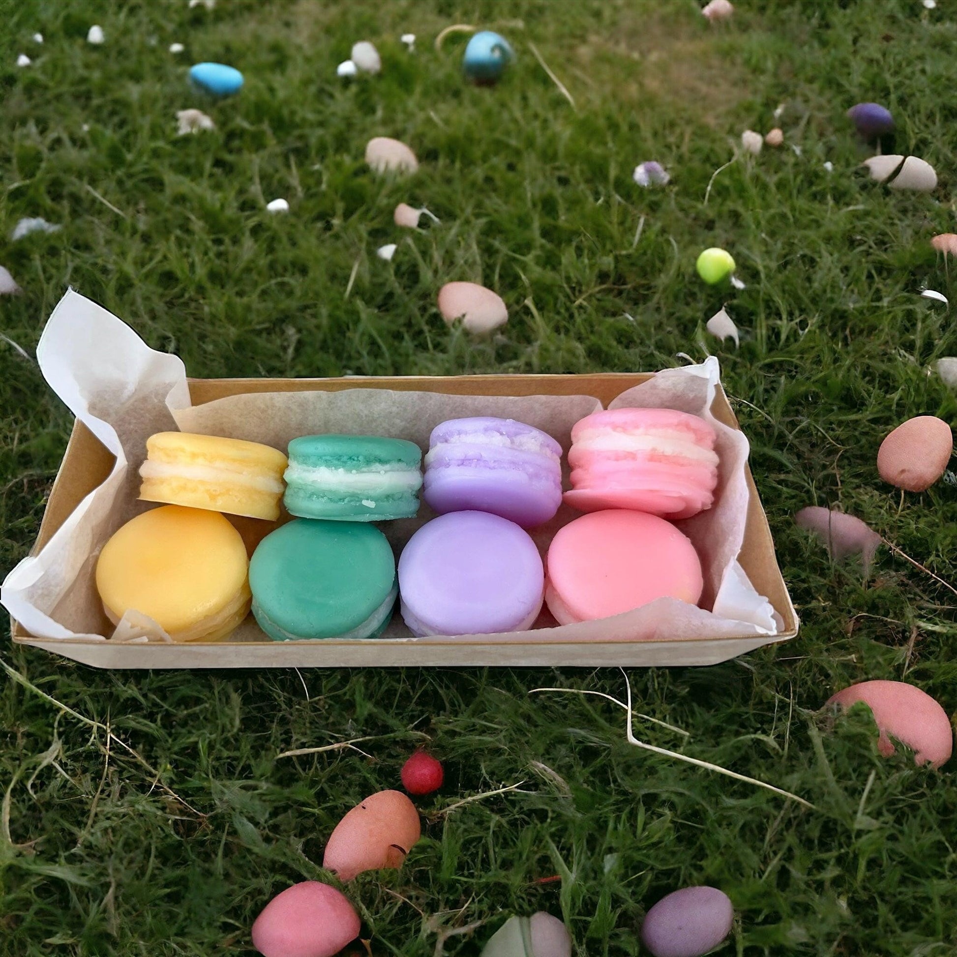 Doodlations Coffee Bar & Boutique Easter Macaroon Wax Melts in pastel yellow, teal, lavender, and pink, arranged in a box on grass with Easter eggs.