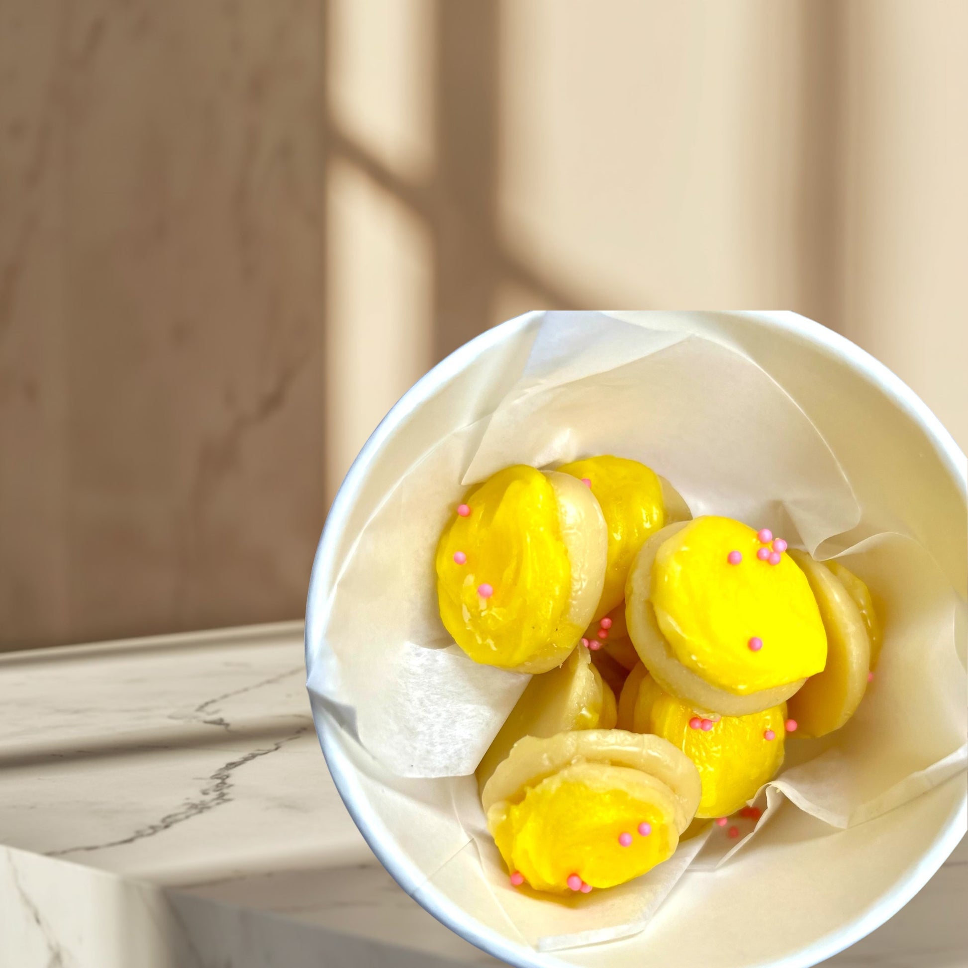 Doodlations Coffee Bar & Boutique Lemon Sugar Cookies wax melts, shaped like macarons, with yellow frosting and pink sprinkles.