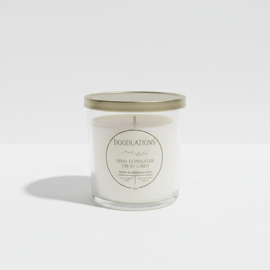 Doodlations Coffee Bar & Boutique Odor Eliminator candle in a clear glass jar with a gold lid and fresh linen scent.