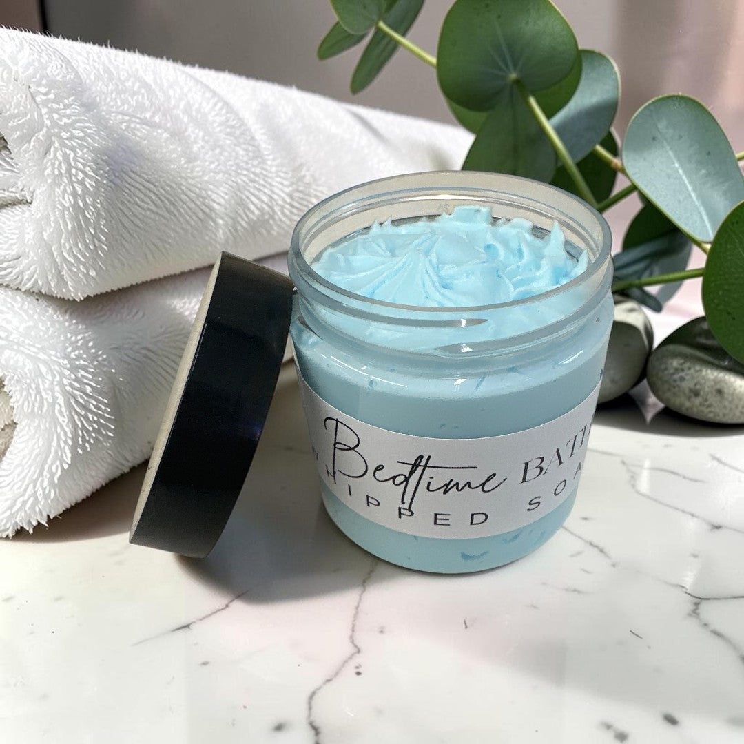 Doodlations Coffee Bar & Boutique Bedtime Bath whipped soap in a blue jar with a white towel and eucalyptus sprig.
