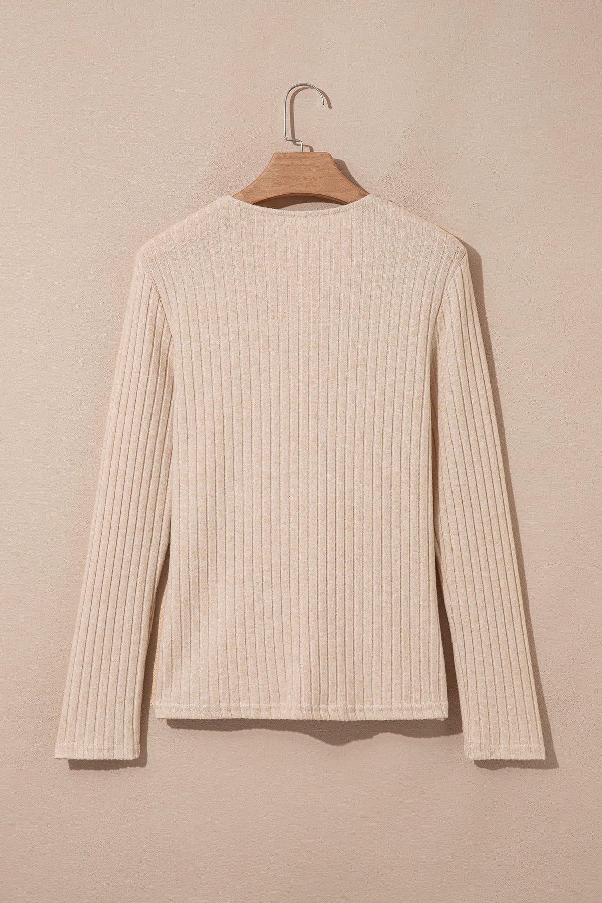 Doodlations Coffee Bar & Boutique apricot ribbed knit long sleeve top hanging on a wooden hanger, back view.