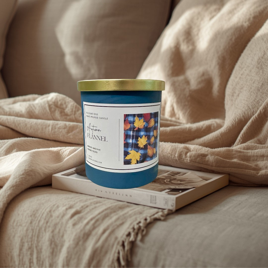 Doodlations Autumn Flannel hand-poured soy blend candle in a teal jar with a gold lid. Features a label with plaid and fall leaves.
