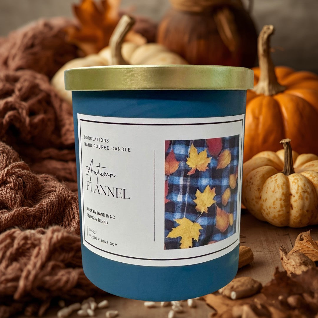 Doodlations Autumn Flannel luxury hand-poured soy blend candle in a teal jar with a gold lid. Features a label with plaid and fall leaves.