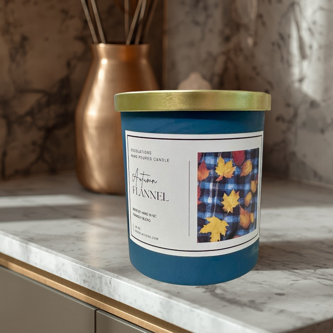 Doodlations Autumn Flannel hand-poured soy blend candle in a teal jar with a gold lid. Features a label with plaid and fall leaves.